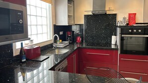 A modern kitchen with red cabinets, a black granite countertop, a built-in oven, and a coffee maker.