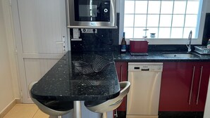 A kitchen with a black countertop, stainless steel appliances, and red cabinets.