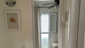A hallway with a ceiling fan, a framed artwork, a bed with a white bedspread, and a bathroom with a shower curtain.