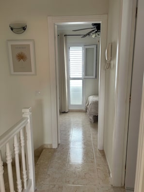 A hallway with a ceiling fan, a framed artwork, a bed with a white bedspread, and a bathroom with a shower curtain. - Beautiful Superior Deluxe Home/Private sun Terrace open views 5gwifi+Netflix tv+ (municipal de mogan, ARGUINEGUIN)