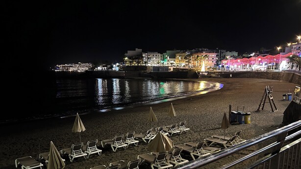 A beachside promenade with rows of sun loungers and umbrellas, a railing, and buildings in the background. - Superior Deluxe Vacation Home with open views Privat sun Terrace & 5G WiFi (municipal de mogan, ARGUINEGUIN)