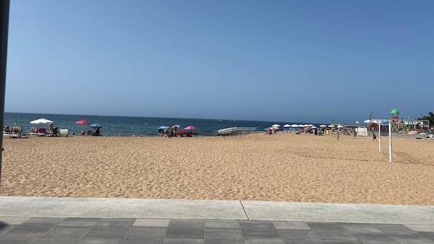 A beach with a clear sky, a sandy shore, and a few umbrellas.