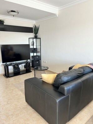 Una sala de estar moderna con un sofá de cuero negro, un televisor de pantalla plana, una mesa de centro de vidrio y un mueble de entretenimiento negro.