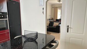 A kitchen with a black countertop, a red oven, and a black refrigerator. There is a dining table with a chair and a black chair with a woven backrest. A white door is visible in the background. - Superior Deluxe Vacation Home with open views Privat sun Terrace & 5G WiFi (municipal de mogan, ARGUINEGUIN)