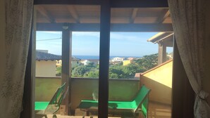 Un balcon avec deux chaises vertes et une table, donnant sur un quartier résidentiel avec des maisons et offrant une vue dégagée sur la mer.