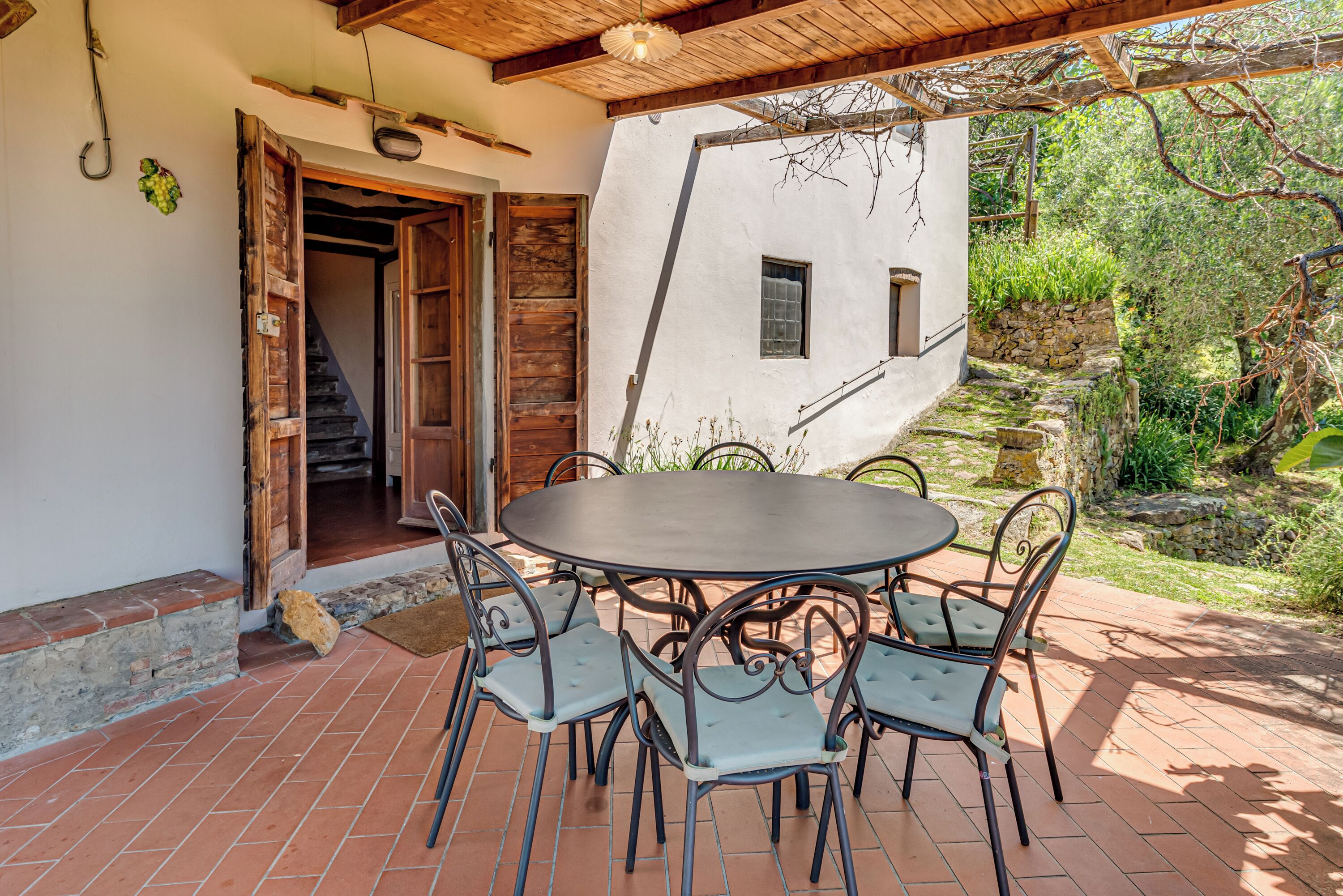 A patio with a round table and chairs, a wooden door, and a stone staircase leading to a white building.