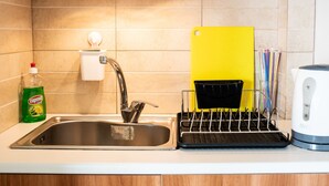 Une cuisine équipée d’un évier en acier inoxydable, d’une planche à découper jaune, d’un égouttoir, d’une bouilloire et d’une bouteille de liquide vaisselle.