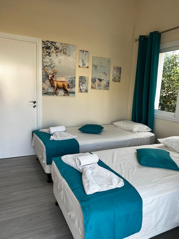 A hotel room with two beds, teal bedding, white towels, and wall art depicting deer and nature scenes. - Lucky 5 (Paralimni)