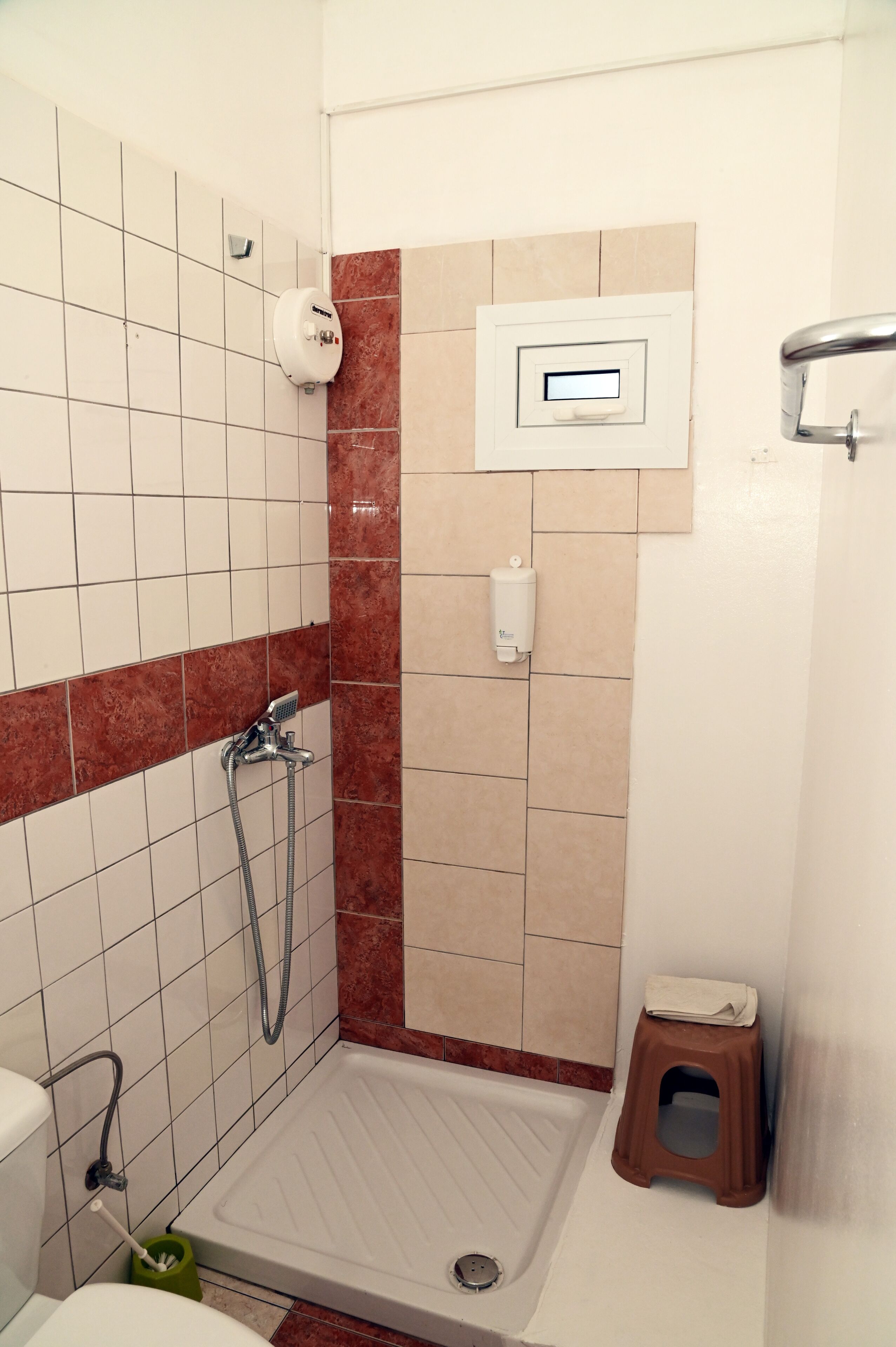 Un espace douche équipé d’un pommeau de douche à main, d’un panneau de commande fixé au mur et d’un petit tabouret.