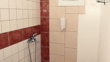 Un espace douche équipé d’un pommeau de douche à main, d’un panneau de commande fixé au mur et d’un petit tabouret.