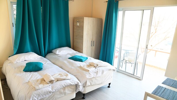 Une chambre avec deux lits, des rideaux de couleur turquoise, une armoire et une vue sur l’extérieur.