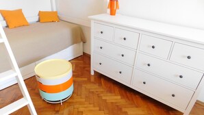 Ein Schlafzimmer mit einem Bett, einem Schminktisch, einer Lampe und einem Papierkorb.