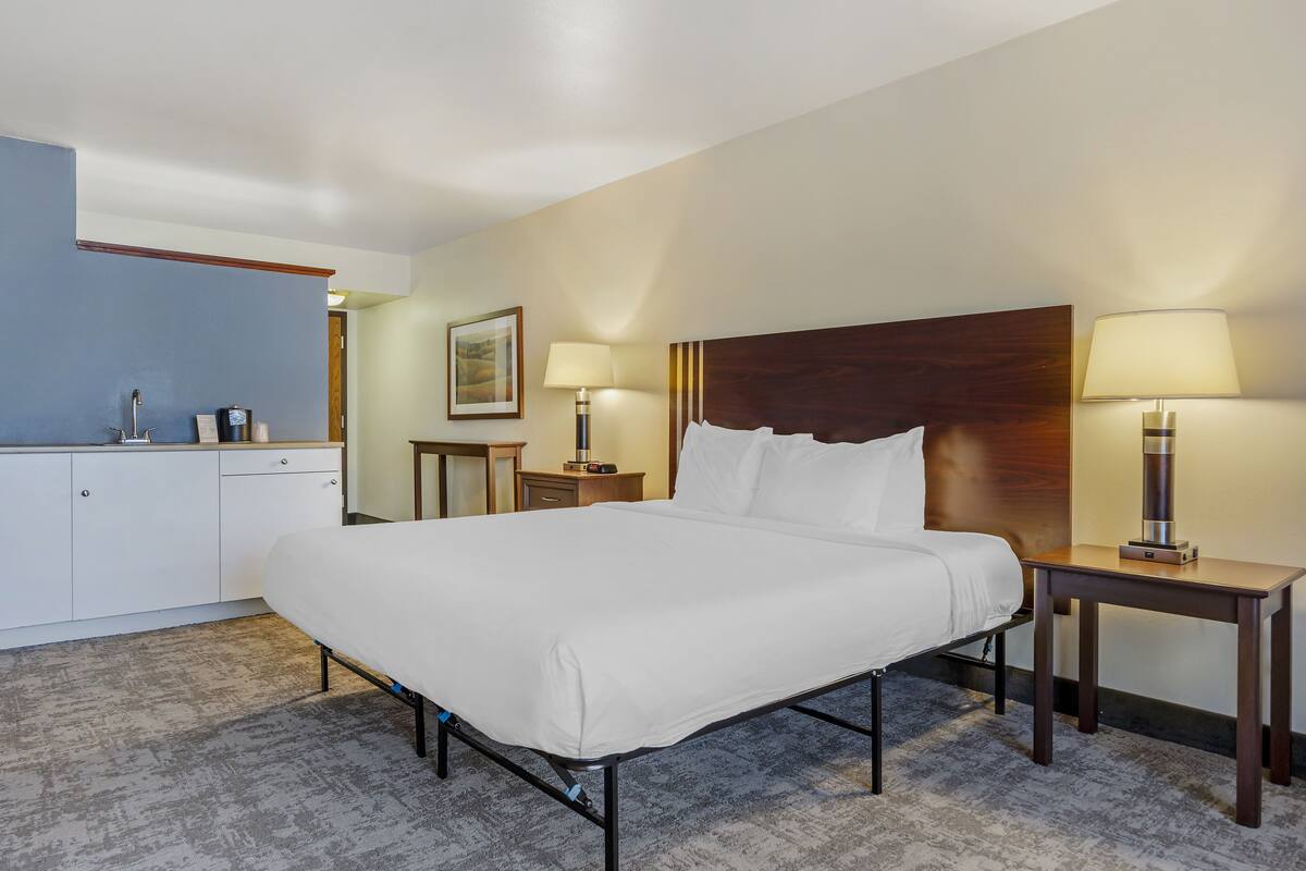 A hotel room with a large bed, bedside tables with lamps, a small desk, and a cabinet.