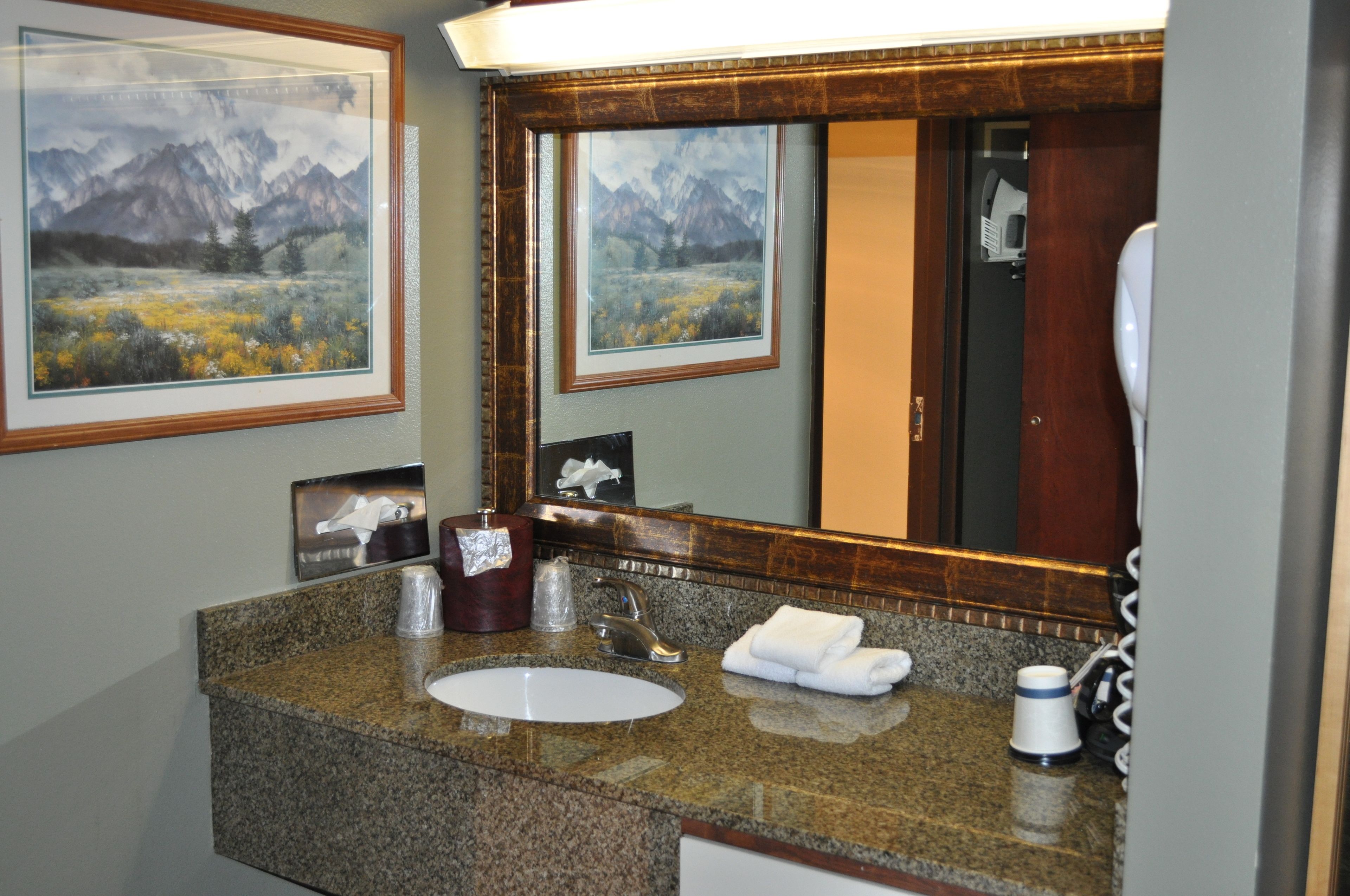 A bathroom with a granite countertop, a sink, a mirror, and framed landscape paintings.