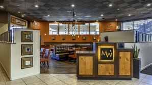 A modern restaurant interior with a central seating area, a wooden reception desk, and framed pictures on the walls. - Seaport Inn and Suites (Lewiston)