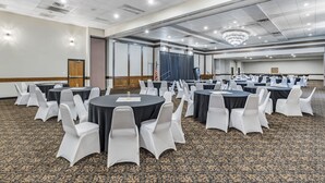A conference room with round tables, white chairs, and a carpeted floor. - Seaport Inn and Suites (Lewiston)