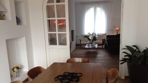 Een eetgedeelte met een houten tafel en stoelen, een witte deur met ruitpanelen, een bank en een salontafel met een plant.