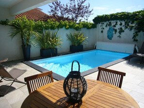 A poolside area with a wooden table, chairs, and a lantern.
