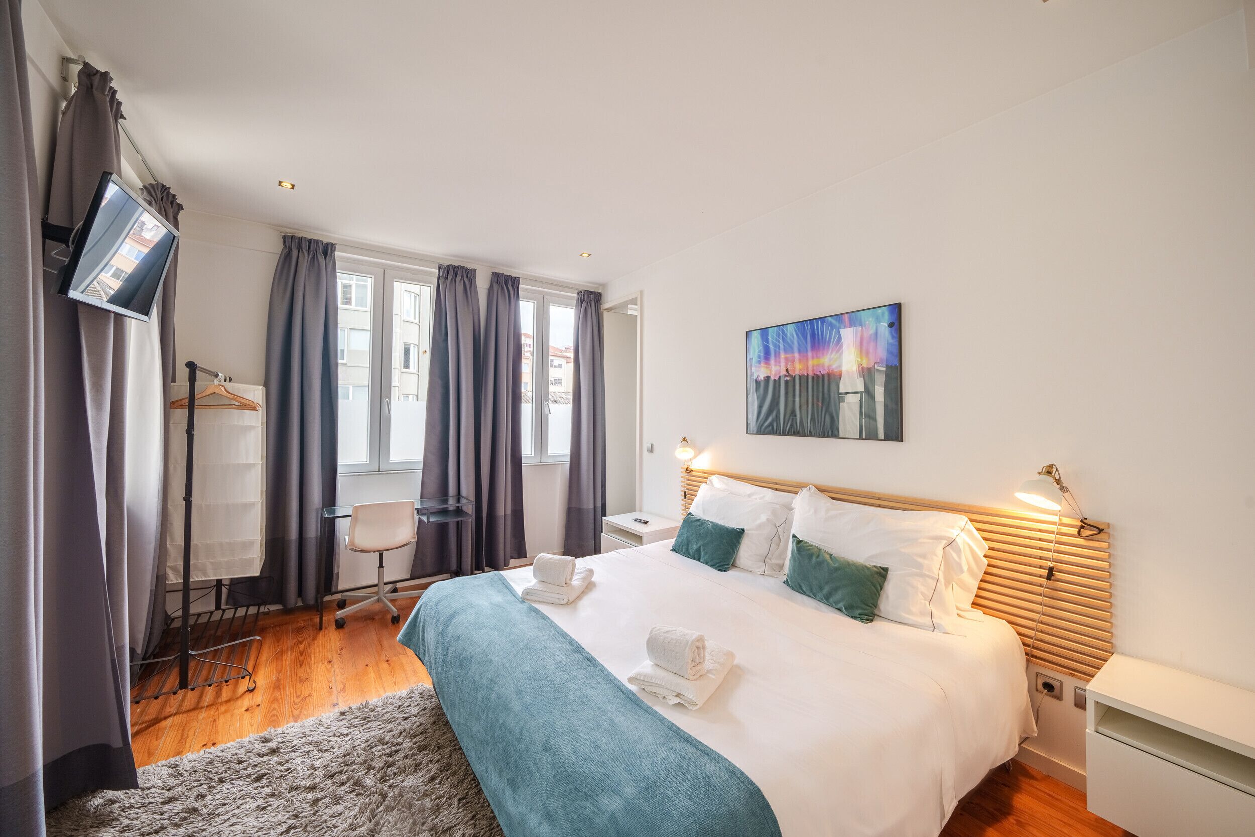 A modern hotel room with a large bed, a desk, a chair, and a TV.