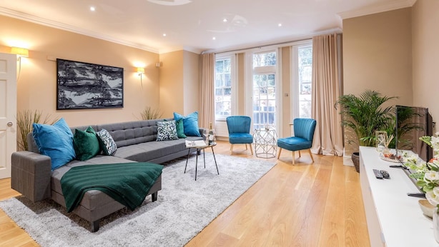 A modern living room with a grey sectional sofa, blue armchairs, and a white coffee table. - Spacious 3 bed Kensington apartment with Patio (London)