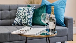 A modern living room with a grey sofa, a small round table with a bottle of champagne and two glasses, and a magazine. - Spacious 3 bed Kensington apartment with Patio (London)