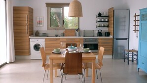 A modern kitchen with wooden cabinets, a built-in washing machine, a dining table with chairs, and a hanging light fixture. - Fab modern garden apartment in idyllic hamlet in natural park. Lovely terraces. (Barbate)