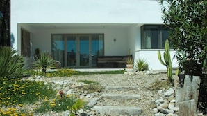 A modern house with a stone pathway leading to a glass door entrance, surrounded by various plants and cacti. - Fab modern garden apartment in idyllic hamlet in natural park. Lovely terraces. (Barbate)