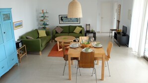 A modern living room with a green sofa, a wooden dining table, and a hanging light fixture. - Fab modern garden apartment in idyllic hamlet in natural park. Lovely terraces. (Barbate)
