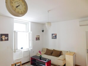 Une pièce comprenant une grande horloge murale, un canapé, une table basse, un meuble et une fenêtre.
