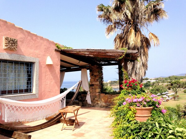 A cozy outdoor seating area with a hammock, a wooden table, and a view of the sea. - Luxury villa with private pool on the beach of Cala Caterina (Villasimius)
