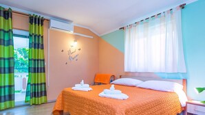 Une chambre à coucher avec une couvre-lit matelassé orange, une table de chevet en bois et une fenêtre ornée de rideaux légers.