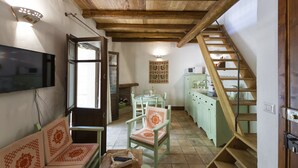 A spacious living area with a wooden staircase, a dining table, and a television. - "Domu Irde: from a ruin a dream" (Baunei)