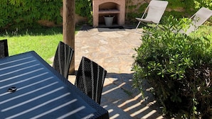 Een terras buiten met een bakoven voor pizza, een tafel met stoelen en een pergola erboven.
