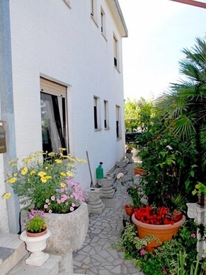 Steps lead up to a charming residential building surrounded by a lush courtyard with potted plants and flowers.