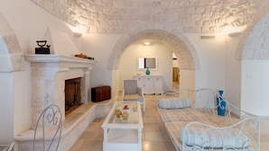 A cozy room with a stone fireplace, a sofa, a small table, and a television in the background. - Luxury trullo, Private  Pool, Air con, Private Tennis Court, Pizza Oven (castellana grotte)