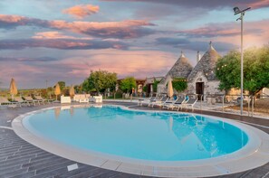 A swimming pool with lounge chairs, a stone building with conical roofs, and a sunset sky. - Luxury trullo, Private  Pool, Air con, Private Tennis Court, Pizza Oven (castellana grotte)