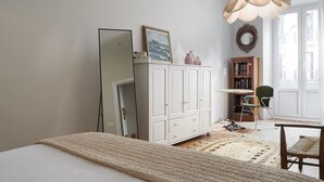 A bedroom with a bed, a white wardrobe, a mirror, a green chair, and a bookshelf. - Always Easy I Catedral (San Sebastián/Donostia)