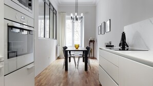 A modern kitchen with white cabinetry, a wooden floor, a dining table with chairs, and a chandelier. - Always Easy I Catedral (San Sebastián/Donostia)
