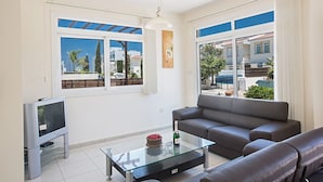 A modern living room with a glass coffee table, a grey sofa, and a television. - Villa Merly, Modern 3BDR Protaras Villa with Pool, Close to Fig Tree Bay Beach (5295)