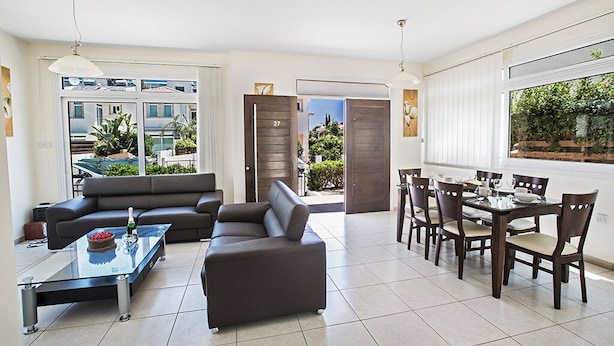 A modern living room with a sofa, a glass coffee table, and a dining area with a table and chairs. - Villa Merly, Modern 3BDR Protaras Villa with Pool, Close to Fig Tree Bay Beach (5295)