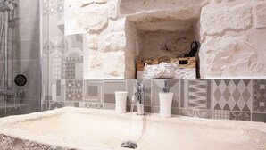 Casa de banho com lavatório de pedra, espelho e parede revestida a azulejos.