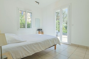 A bedroom with a bed, a nightstand, a radio, and a view of the outdoors through a door.