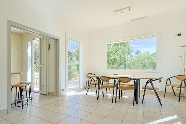 A bright room with a large window, a dining table with chairs, and a door leading outside.