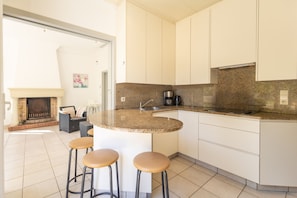A kitchen with a granite countertop, white cabinets, and a built-in stove. There are two stools and a coffee maker on the counter.