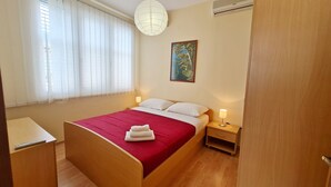 Een hotelkamer met een bed, nachtkastjes, een lamp, een schilderij en een raam met gordijnen.