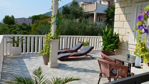 Een balkon met twee lounge fauteuils, een tafel en bloempotten.