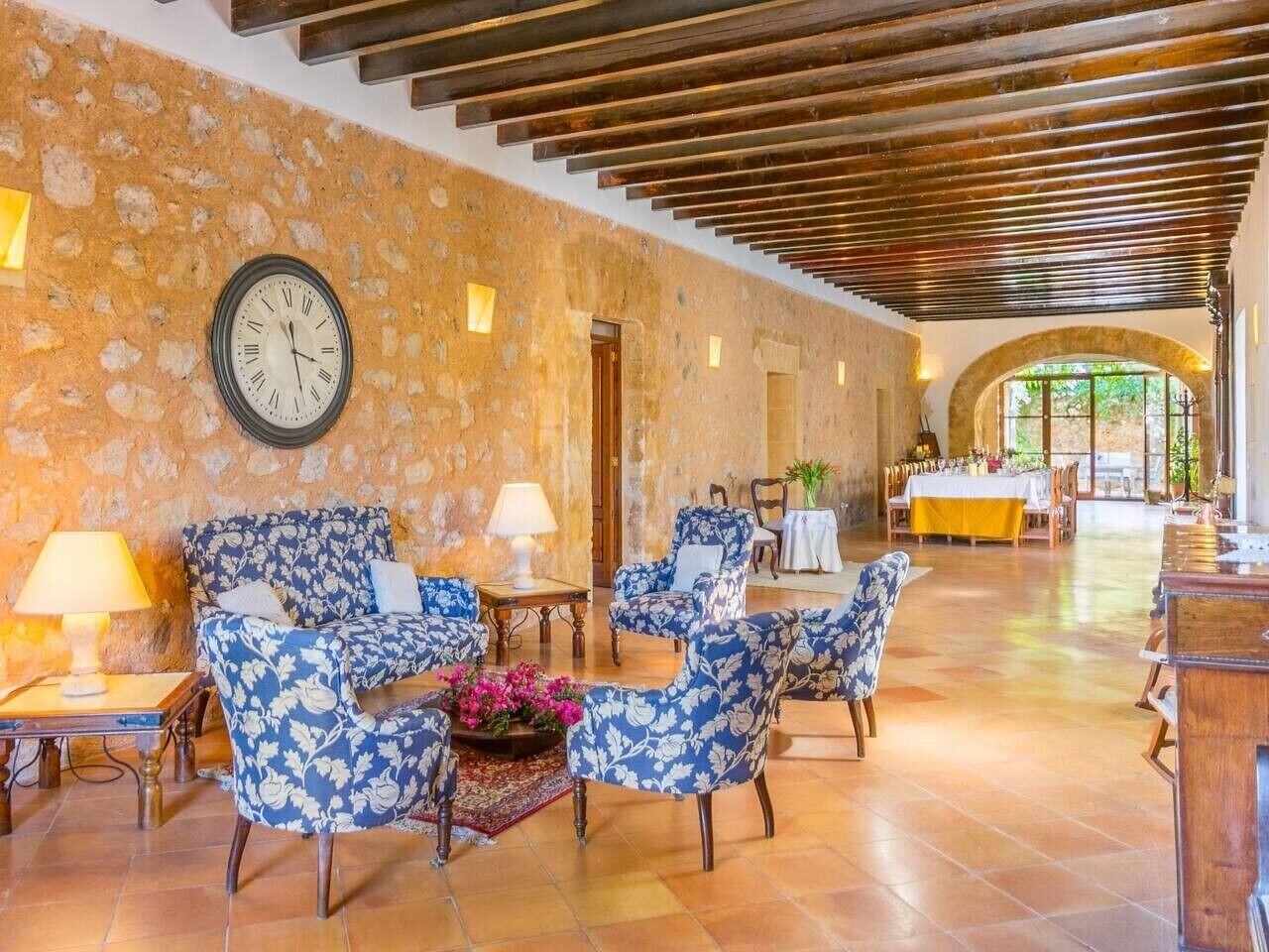 A spacious lobby with a stone wall, a clock, and blue floral armchairs.