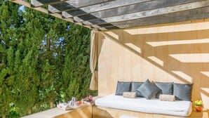 A modern outdoor seating area with a sofa and a table, surrounded by a wooden deck and a backdrop of dense green foliage.