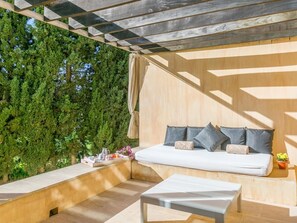 A modern outdoor seating area with a sofa and a table, surrounded by a wooden deck and a backdrop of dense green foliage.