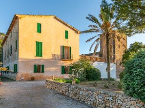 A two-story building with a stone wall in front, a palm tree, and a clear sky. - Historic Finca in Mallorca with Pool for 12 Guests (Andratx)